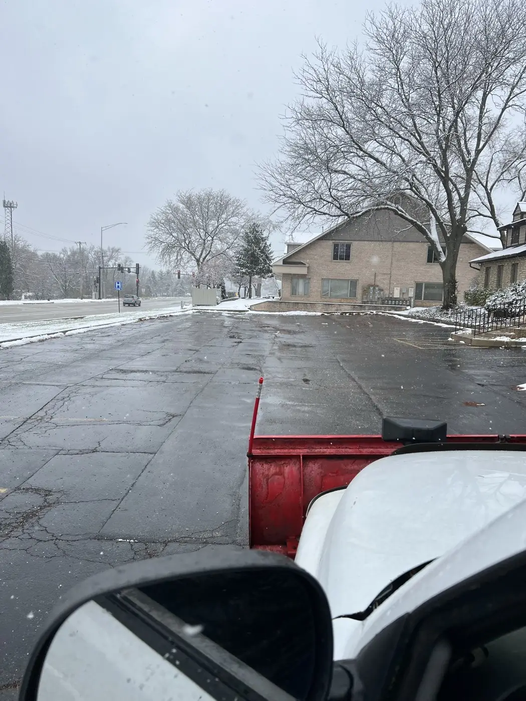 View from an Arctic Fox Snow Services truck: the red plow blade over a cleared commercial parking lot